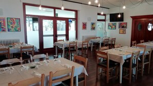 A dining area with multiple tables set for service, wooden chairs, and artwork on the walls. - Hotel Rossi (Domagnano)