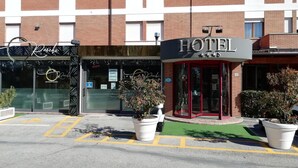 A hotel with a red entrance, a restaurant named "Racchi" across the street, and potted plants in front. - Hotel Rossi (Domagnano)