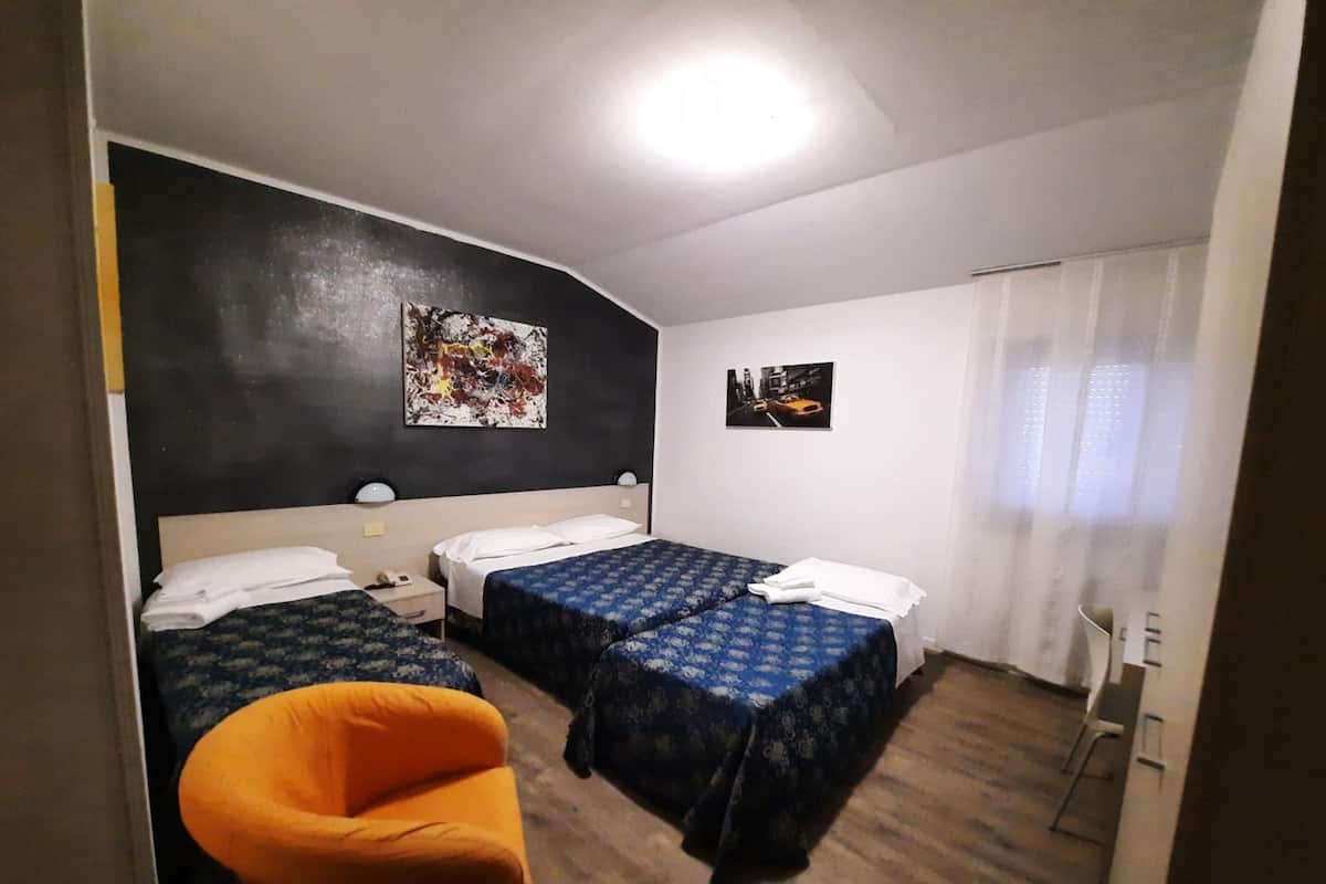 A hotel room with two beds, a chair, and artwork on the walls.