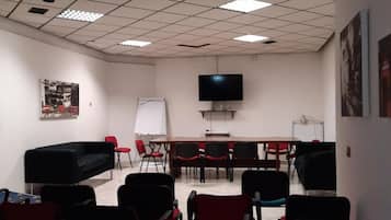 Uma sala de conferência com uma mesa grande, várias cadeiras, um quadro branco e uma televisão na parede.