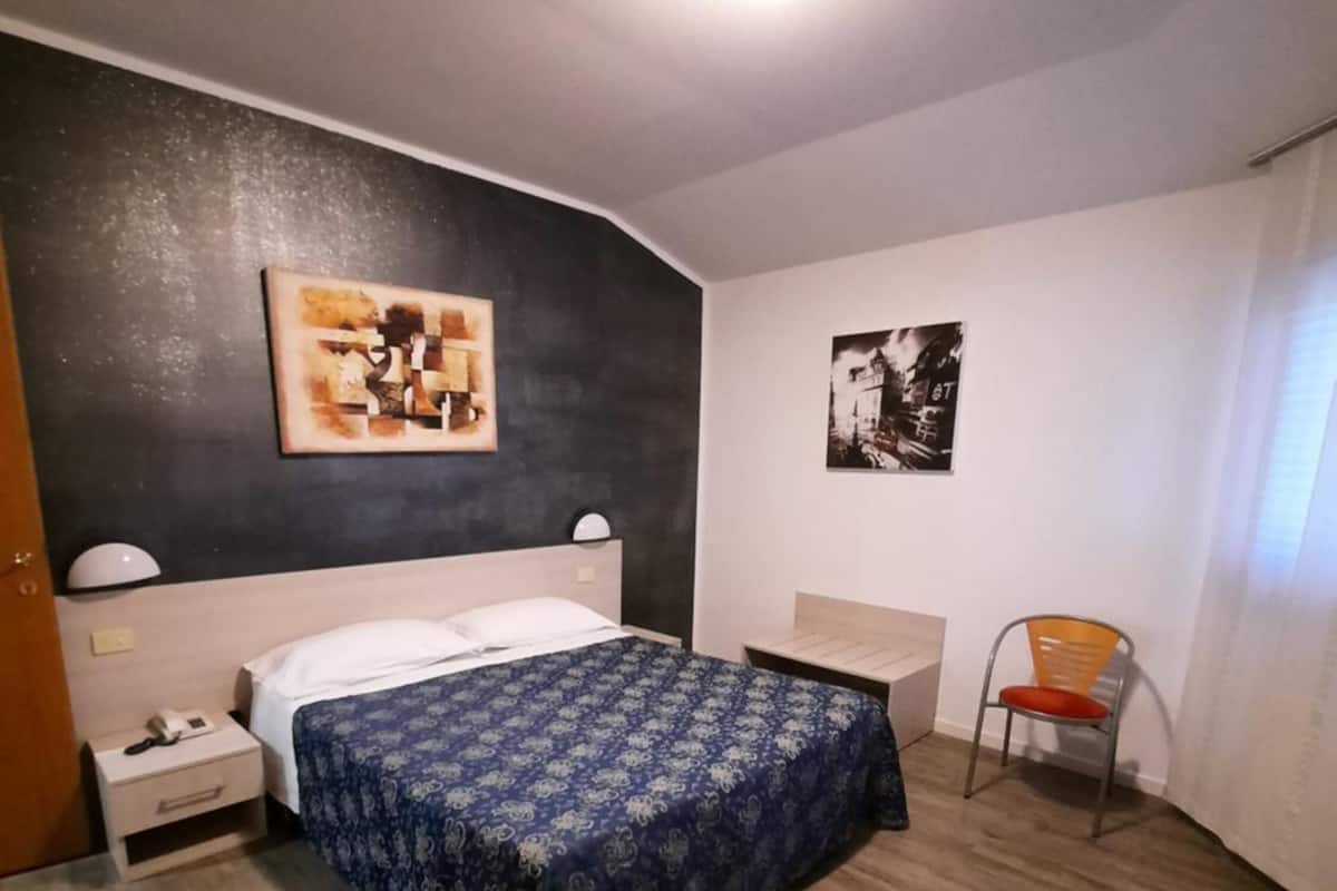 A bedroom with a bed, a nightstand, a chair, and a wall with two artworks.