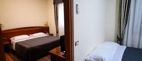 A hotel room with two beds, wooden headboards, a small table, and a bedside lamp.