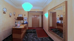 A hotel reception area with a marble floor, a large mirror, a chandelier, and clocks on the wall. - Hostal Regio (Madrid)