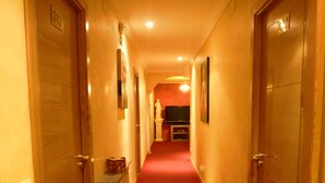 A hotel hallway with a red carpet, wooden doors, and a television mounted on the wall. - Hostal Regio (Madrid)