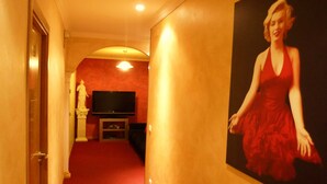 A hallway with a red carpet, a painting of a woman in a red dress, and a television set against a red wall. - Hostal Regio (Madrid)
