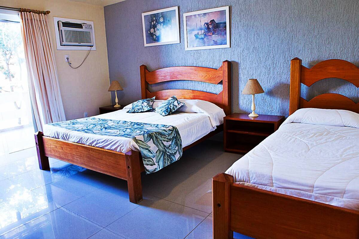 Ein Hotelzimmer mit zwei hölzernen Betten, einem Nachttisch, einer Lampe und einer Wandklimaanlage.