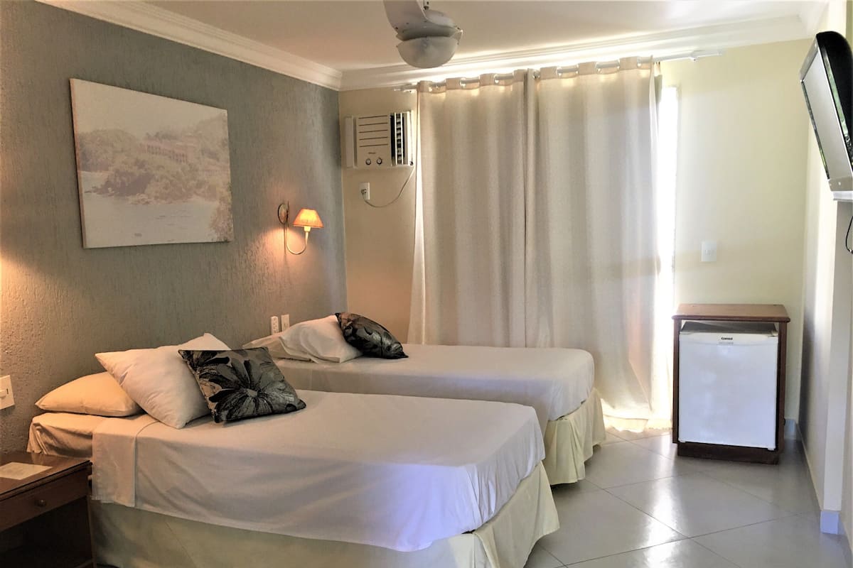 Ein Hotelzimmer mit zwei Betten, einem kleinen Kühlschrank, einer Wandheizung und einem Bild an der Wand.