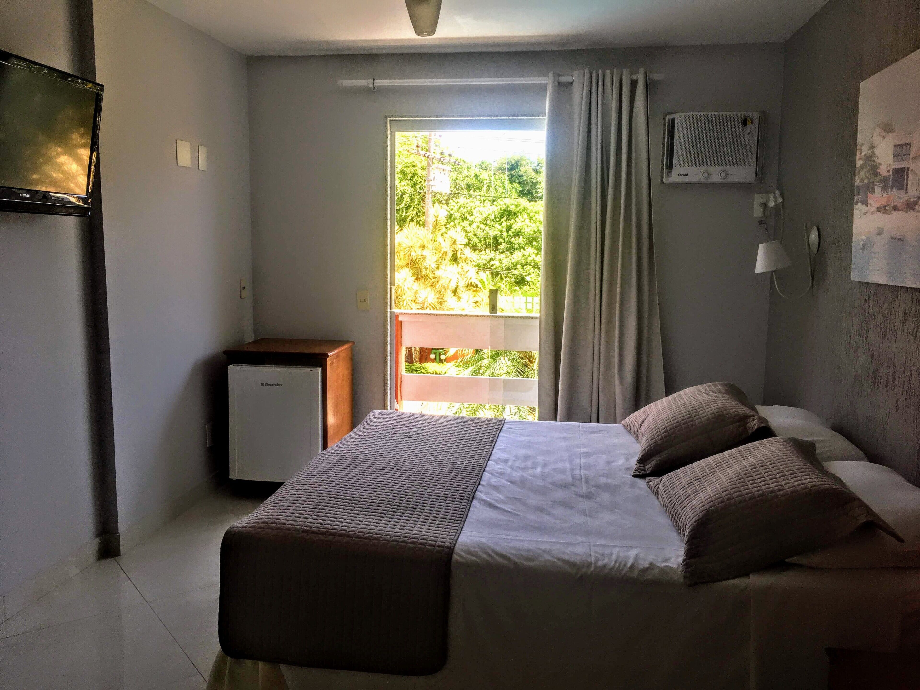 A bedroom with a bed, a small desk, a window with curtains, and an air conditioning unit.