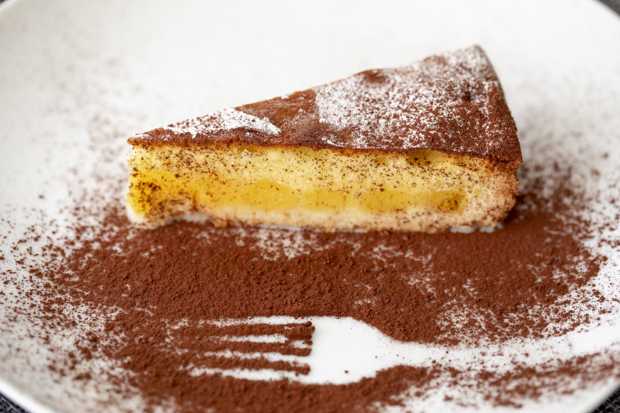 Une part de tiramisu sur une assiette, saupoudrée de cacao.