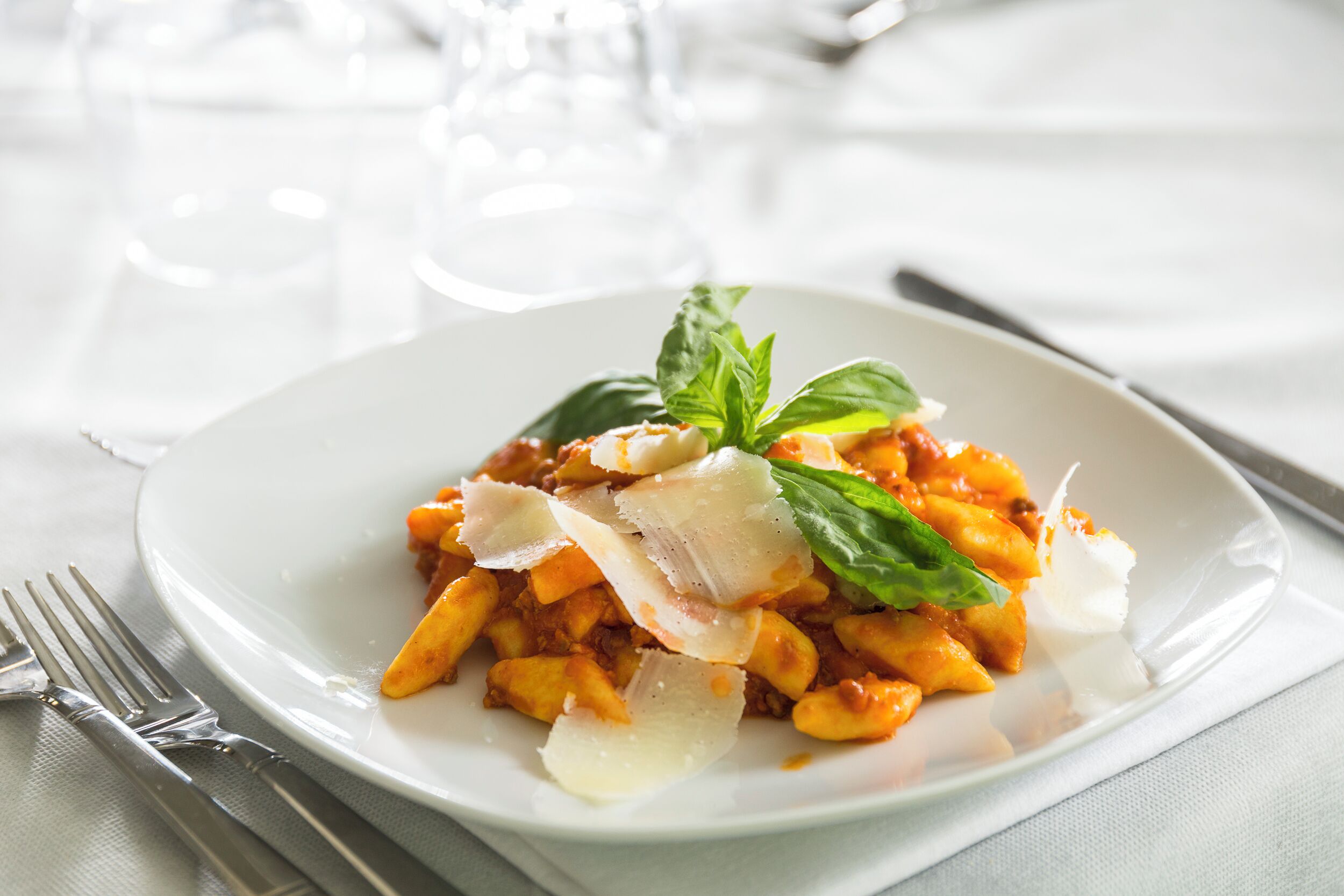 Une assiette de pâtes, garnie de fromage et de basilic, est posée sur une assiette blanche.