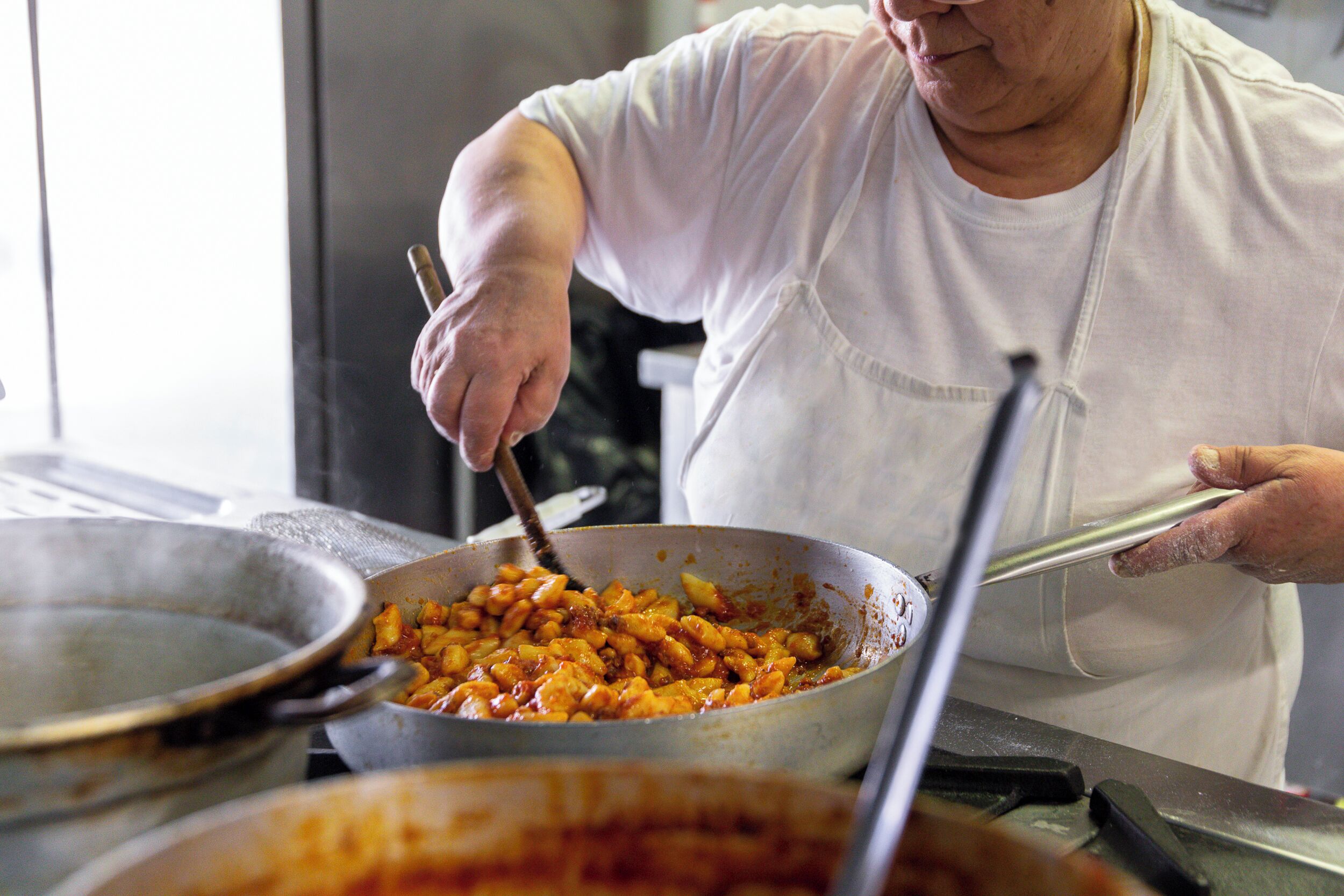 A person cooking in a kitchen with a large pot and a pan.