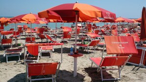 Ein Strand mit vielen roten Sonnenschirmen und Liegestühlen, einige mit dem Schriftzug "HOTEL" und "MEDIBERANEO".