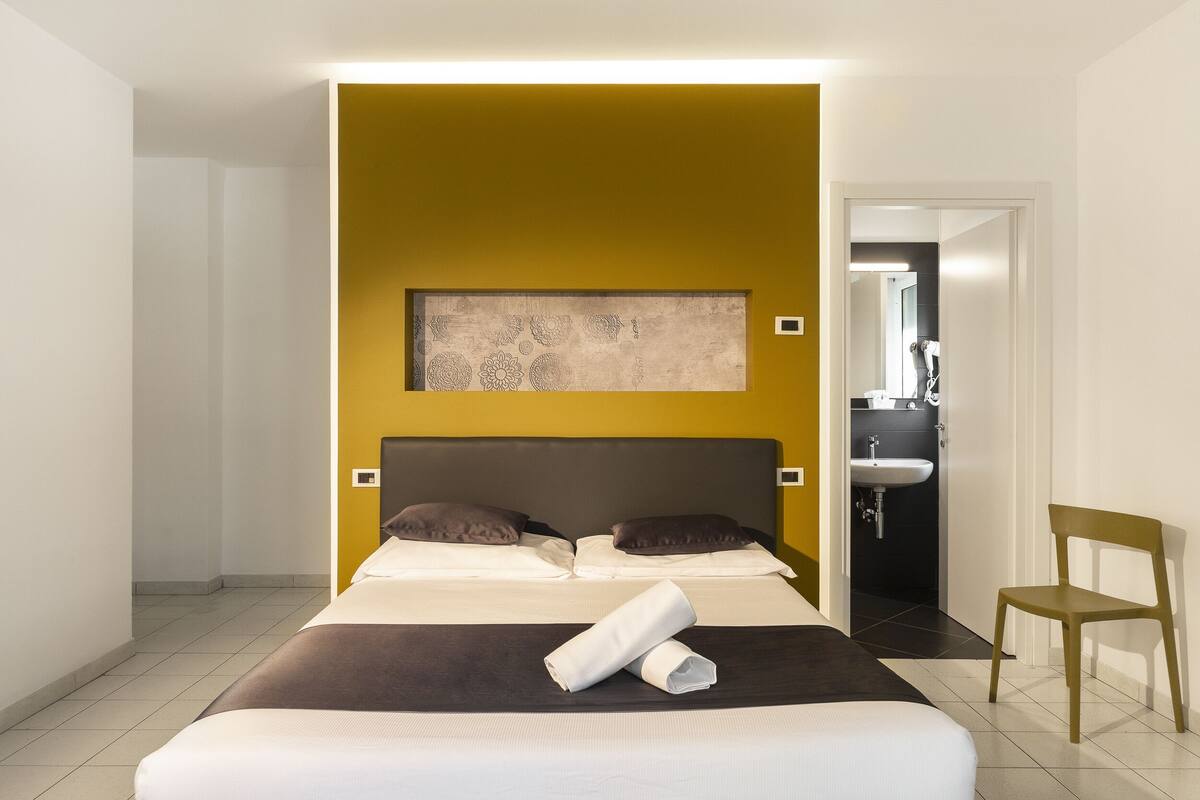 Ein Hotelzimmer mit Bett, Sessel, einem Bild an der Wand und einem durchgegangene Tür erkennbaren Badezimmer.