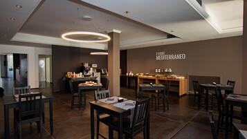 Een modern restaurantinterieur met meerdere eettafels en stoelen, een keukenhoek en een muur met de tekst 'FOOD: MEDI TERRANEO'.