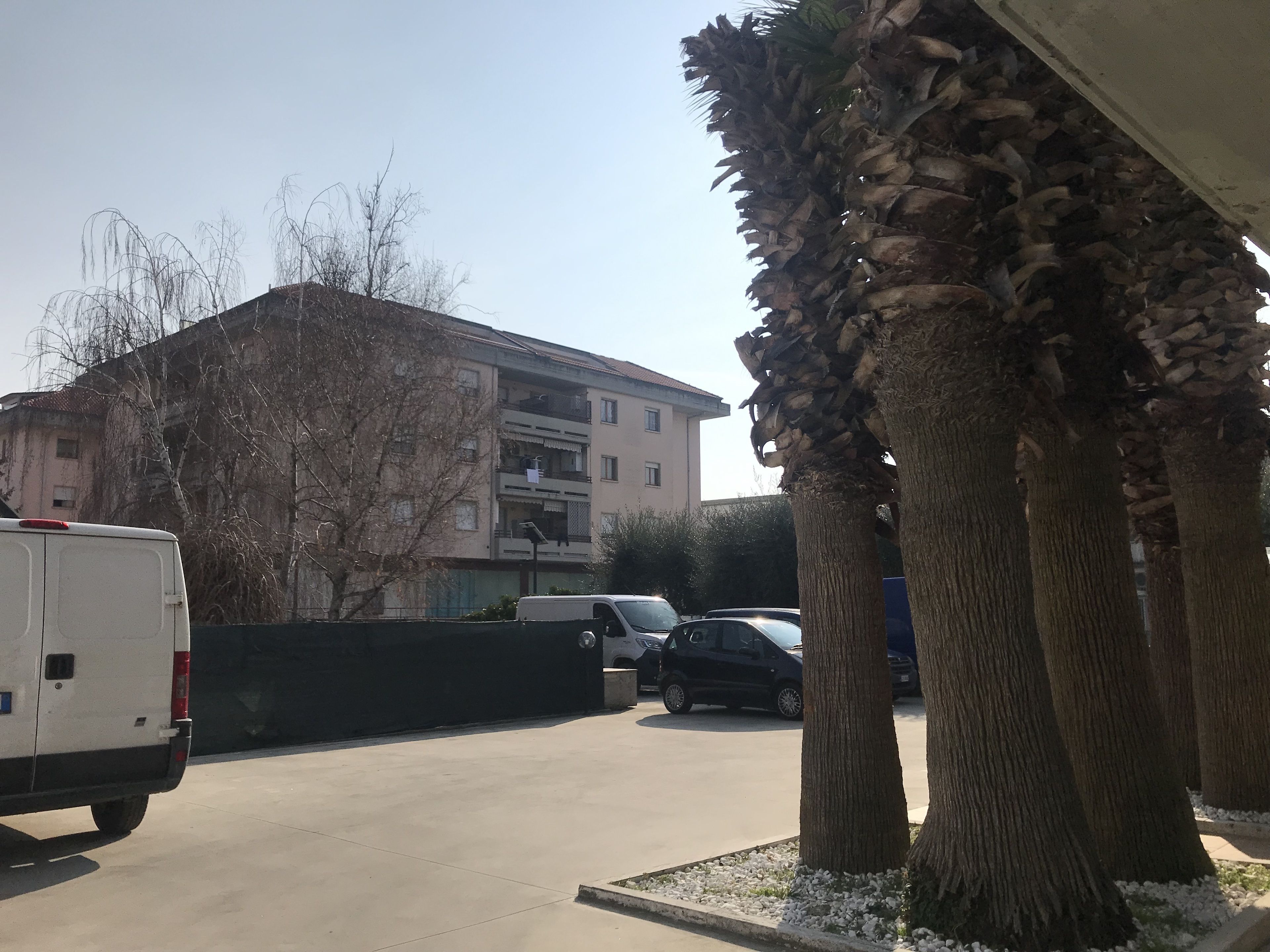 Ein Parkplatz mit einem weißen Lieferwagen, mehreren Autos und einem Gebäude mit Balkonen.