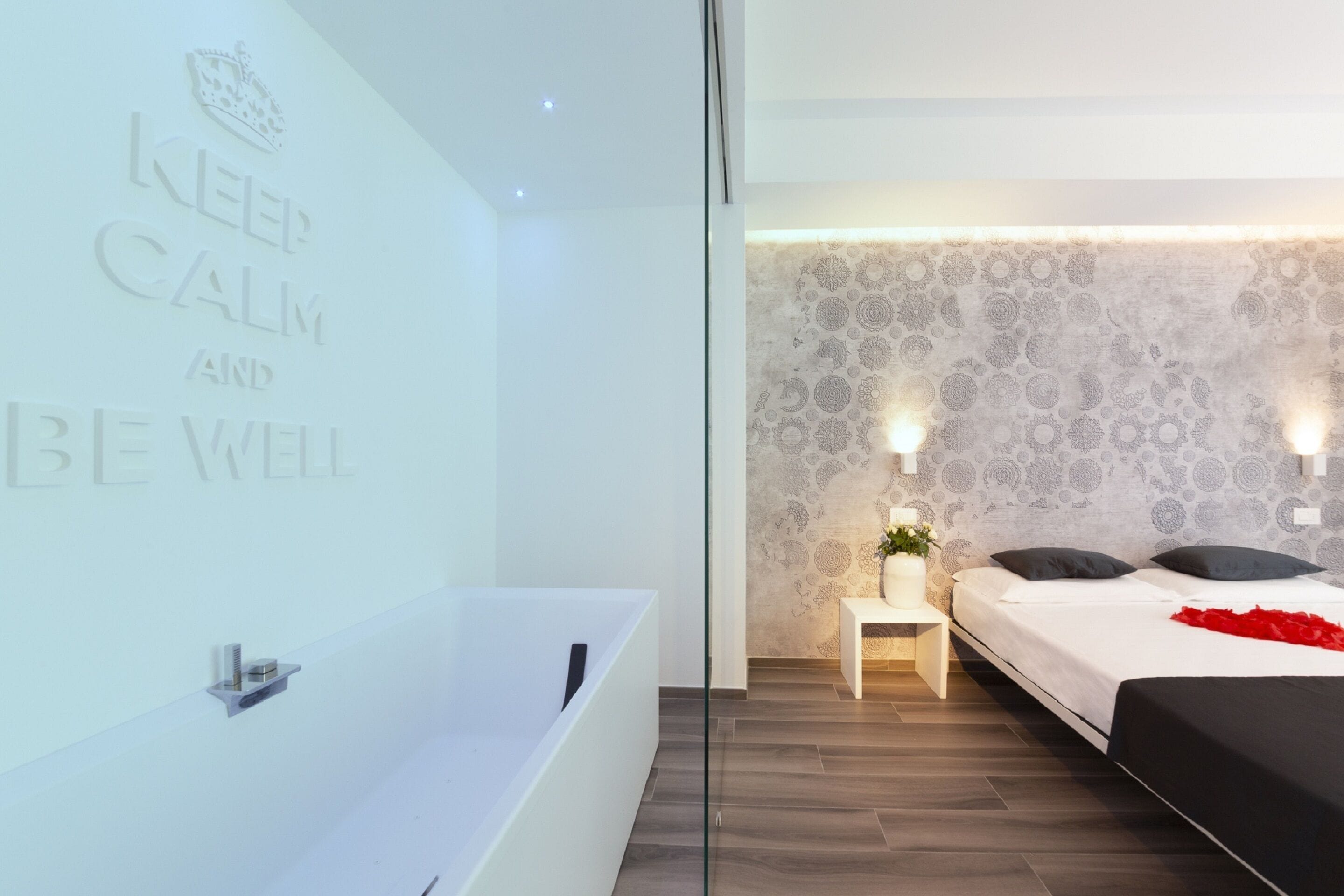 A modern bedroom with a large bathtub, a bed with black bedding, and a wall with a calming message.