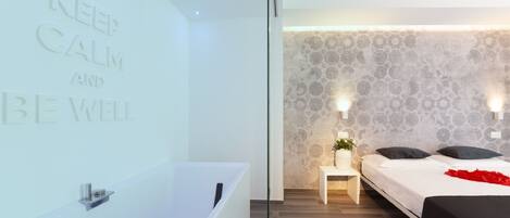 A modern bedroom with a large bathtub, a bed with black bedding, and a wall with a calming message.