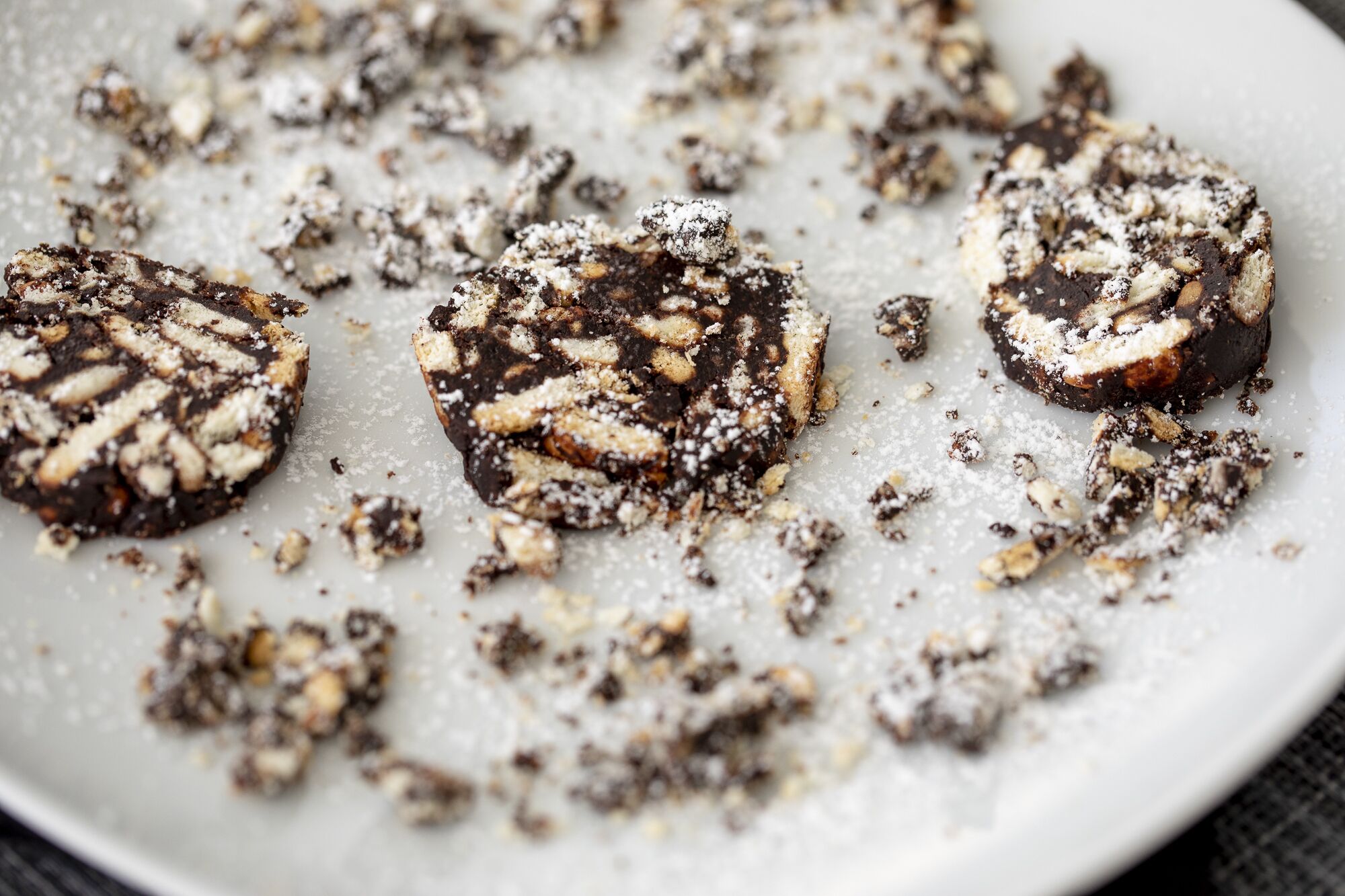 A plate with three chocolate desserts dusted with powdered sugar.