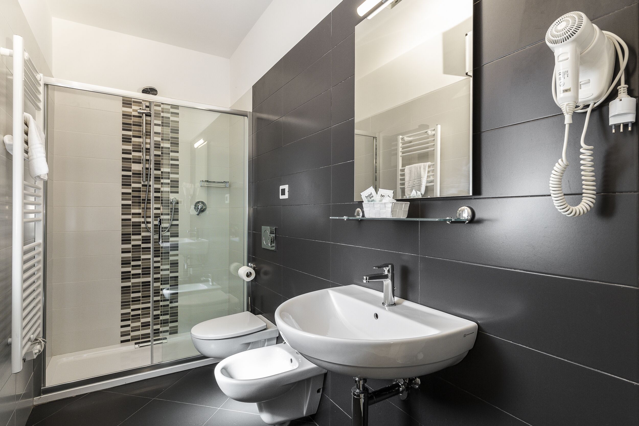 A modern bathroom with a glass shower enclosure, a white sink, and a hairdryer mounted on the wall.