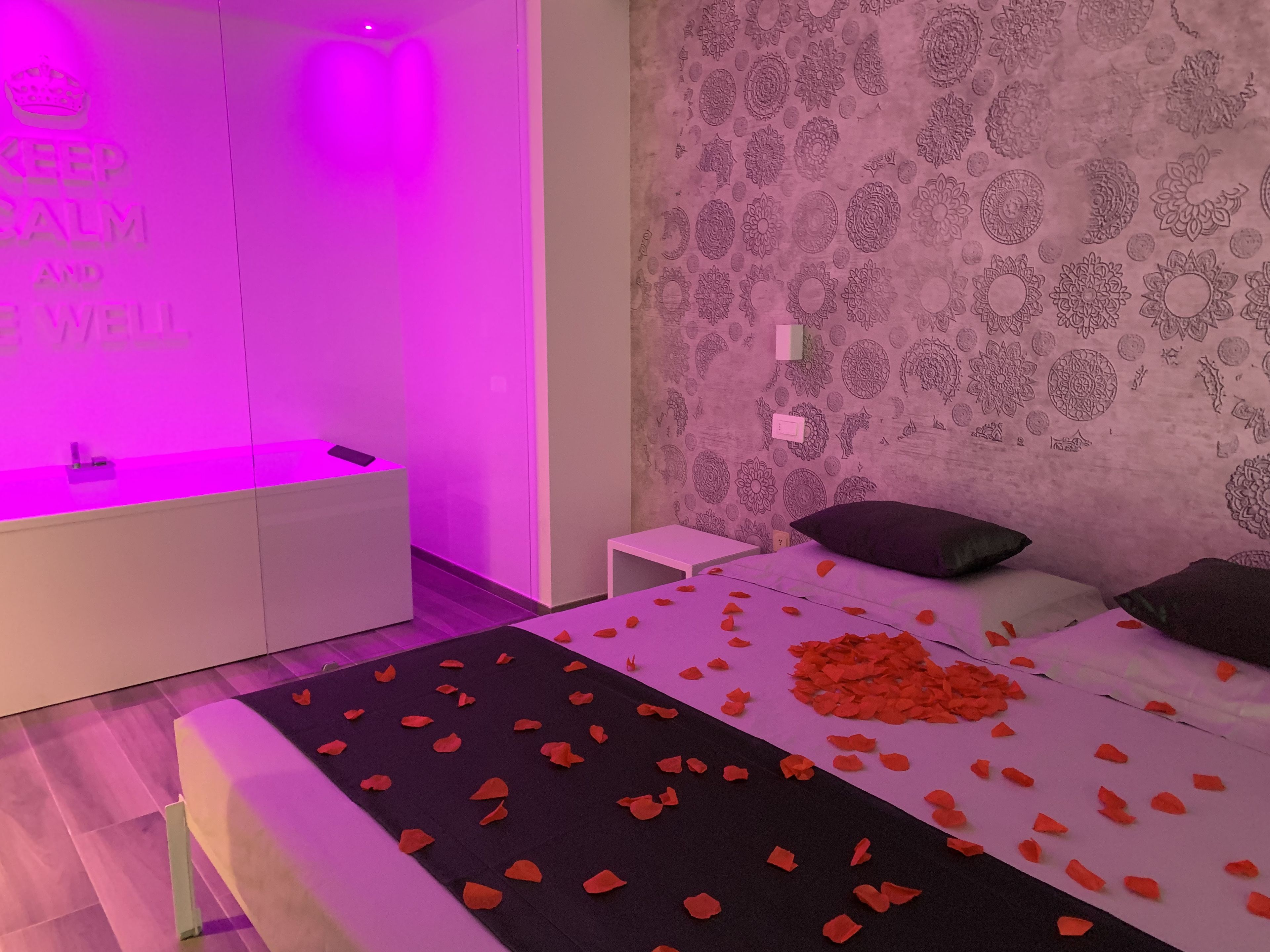 Un dormitorio con una cama cubierta de pétalos de rosa, una mesita de noche blanca y una mesita auxiliar.