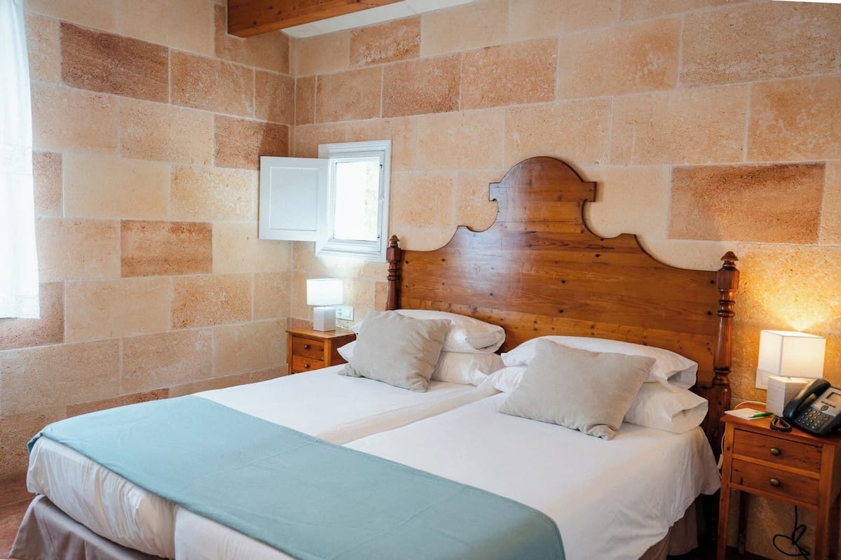 A double bed with a wooden headboard, two bedside tables, a nightstand, and a wall-mounted telephone.