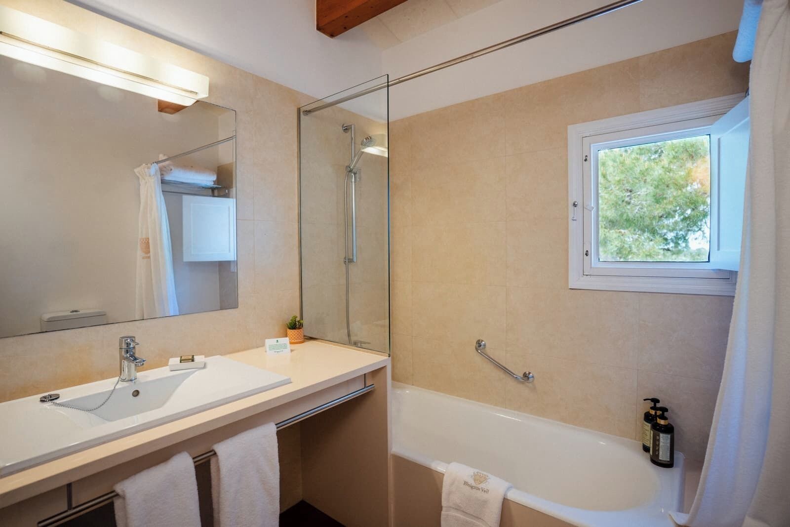 Un baño moderno con un espejo grande, una bañera, una ducha y una ventana que deja entrar luz natural.