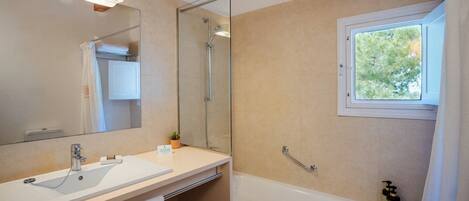 Un baño moderno con un espejo grande, una bañera, una ducha y una ventana que deja entrar luz natural.