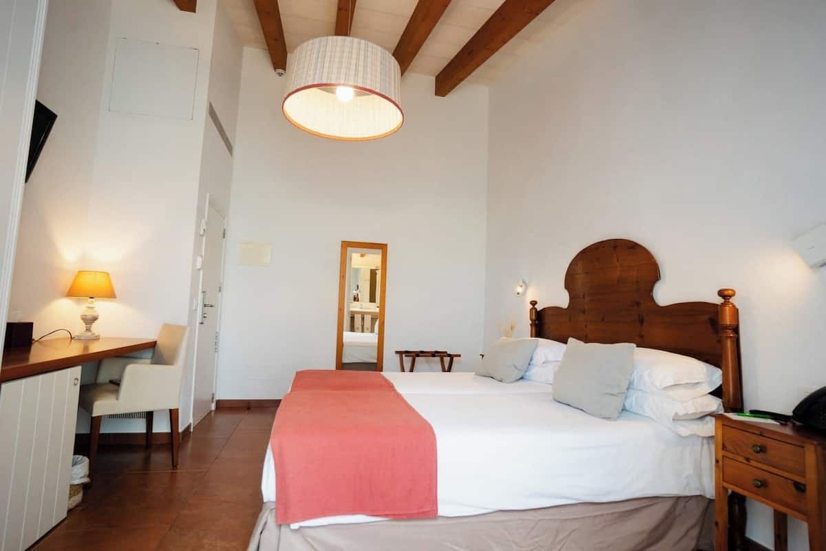 A bedroom with a bed, bedside tables, a desk with a lamp, and a mirror.