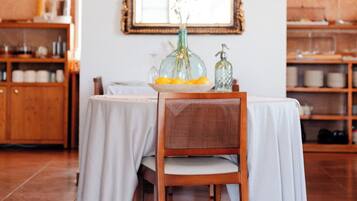 Comedor con una mesa dispuesta para dos, una silla de mimbre, una lámpara decorativa y un espejo sobre la mesa.