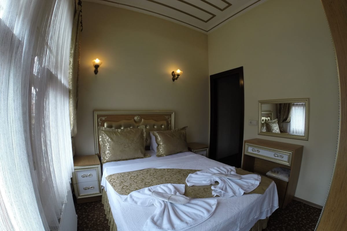 A hotel room with a large bed, two bedside tables, a dresser, a mirror, and a door.