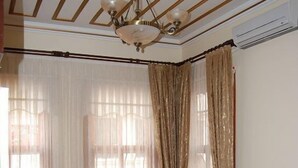 Una sala de estar con un sofá color beige, un tapete estampado, cortinas traslúcidas y un ventilador de techo.
