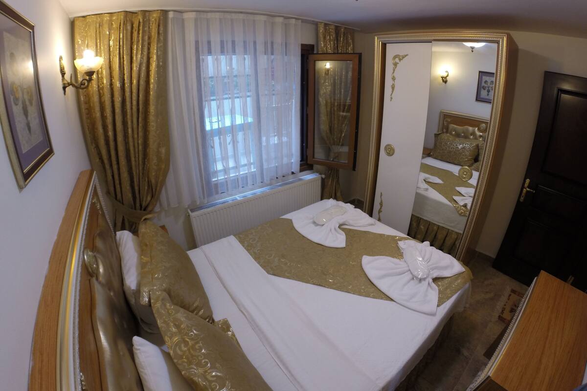 A hotel room with a bed, a radiator, a window with curtains, a mirror, and a door.