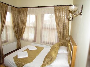 Une chambre d’hôtel avec un lit, des rideaux et un luminaire fixé au mur.