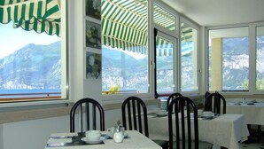 Ein Essbereich mit Tischen für zwei Personen, Stühlen und Blick auf Berge durch große Fenster.