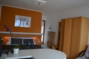 A hotel room with a bed, bedside table, a small desk, a chair, a wardrobe, and a potted plant.