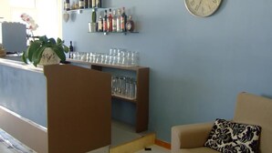 Eine Bar mit Regalen voller Flaschen und Gläsern, einer Uhr und einem Sofa mit einem gemusterten Kissen.