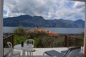 A balcony with a table and chairs, overlooking a lake with mountains in the background.