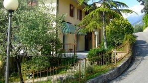 Ein zweistöckiges Haus mit Balkon, umgeben von viel Grün und einer gewundenen Straße.
