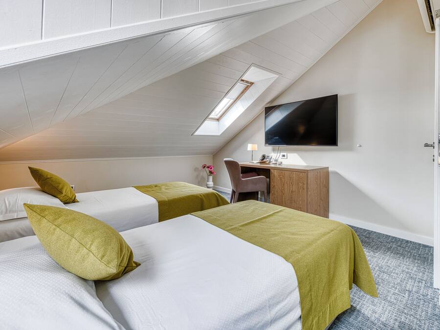 A room with two beds, a desk, a chair, a flat-screen TV, and a skylight.