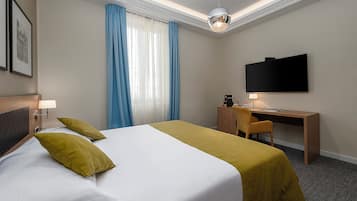 A hotel room with a bed, a desk, a chair, a television, and a window with curtains.