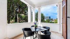 A balcony with a table and chairs, a view of trees and buildings, and a partially visible hotel sign.