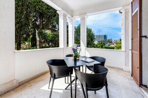Varanda com mesa e cadeiras, vista para árvores e edifícios, e um letreiro de hotel visível em parte.
