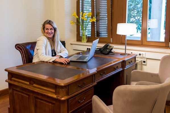 Una persona sentada en un escritorio de madera, con una computadora portátil, un teléfono y un jarrón con flores amarillas.