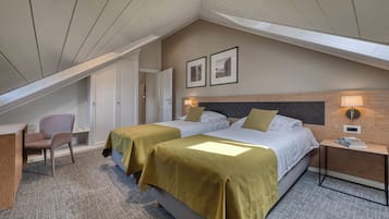 Quarto de hotel com duas camas, uma escrivaninha, uma cadeira e uma pequena mesa com abajur.