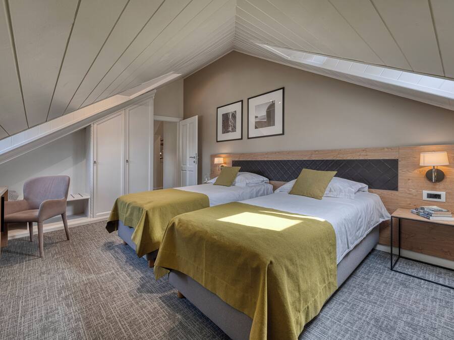Habitación de hotel con dos camas, un escritorio, una silla y una mesita de noche con lámpara.