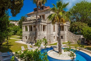 Un edificio de piedra con piscina y sillones de descanso.