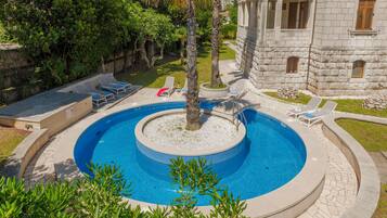 A circular pool with a stone border, surrounded by lounge chairs and a palm tree.
