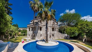 A stone building with a pool, surrounded by trees and a clear sky.