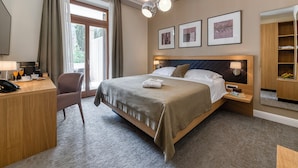 A hotel room with a bed, bedside tables, a desk with a phone, a chair, and a large window with curtains.
