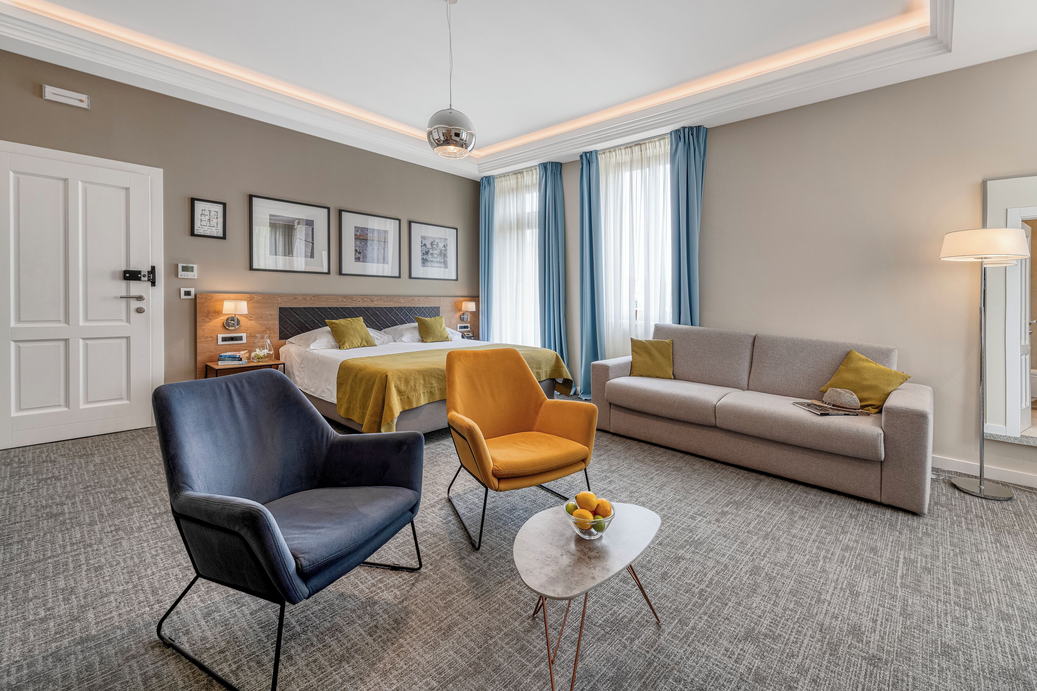 Quarto de hotel com cama, duas poltronas, um sofá, uma mesa de centro e uma escrivaninha com abajur.